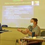 Jennifer Young teaches Drivers Ed to students in class, with one joining from home.