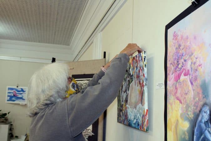OASIS Fine Art and Craft member Sarah Lock hangs student art for he First Friday exhibition at the gallery in Harrisonburg. Photo by Kathleen Shaw/DN-R