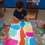 Title: Rainbow Rocket
Size: 24”x18”
Medium: acrylic paint
Description: Kindergarten artists worked in small groups to paint abstract designs directly on a cradled wooden panel. Beginning at the edges and working inward they painted large patches of color as a base layer. Additional layers were created using small blocks of color along with line, shape, and pattern designs. Students were thoughtful in selecting colors that would stand out next to each other, and  they enjoyed talking together about their painting. As the final step in their creative process, the class brainstormed title ideas for their piece then voted for their favorite.
