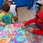 Title: Rainbow Rocket
Size: 24”x18”
Medium: acrylic paint
Description: Kindergarten artists worked in small groups to paint abstract designs directly on a cradled wooden panel. Beginning at the edges and working inward they painted large patches of color as a base layer. Additional layers were created using small blocks of color along with line, shape, and pattern designs. Students were thoughtful in selecting colors that would stand out next to each other, and  they enjoyed talking together about their painting. As the final step in their creative process, the class brainstormed title ideas for their piece then voted for their favorite.
