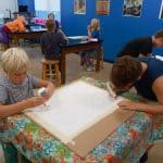 Title: Shapes Collide
Size: 24”x18”
Medium: fabric, acrylic paint
Description: 5th grade students began their batik creation by drawing a simple line and shape design on a small rectangle of paper and tracing it with black Sharpie. After the papers were taped onto a piece of cardboard, covered with wax paper, and finally covered with a large piece of white fabric, students carefully traced their designs with glue onto the fabric. Once the glue was dry, students painted the sections of their design with acrylic paint. When the paint was dry, the glue was washed out of the fabric to reveal the white outline left by the glue. As the final step in their creative process, the class brainstormed title ideas for their piece then voted for their favorite.
